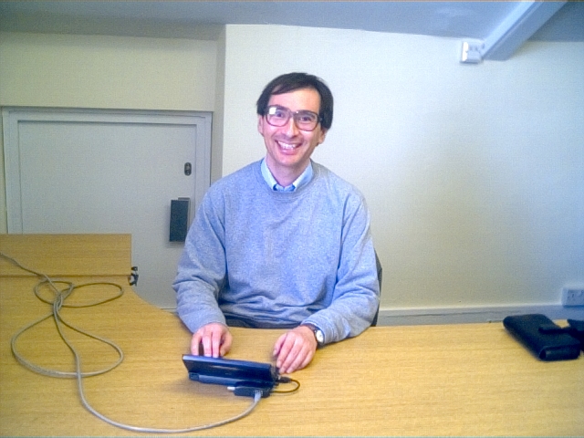 Paul sits at a large desk that's empty apart from a handheld computer with an ethernet cable plugged in and a carry case to one side.